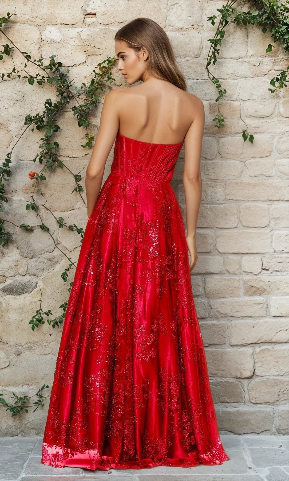A woman with long hair wears the Blondie Nites 4792BN Strapless Glitter Prom Dress, featuring floral patterns, as she stands by a stone wall covered in green vines.